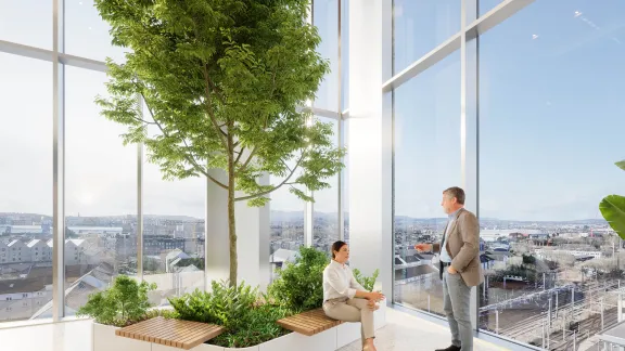 A man and woman stand in a winter garden, surrounded by plants, in front of a large window at New Yards Haymarket.